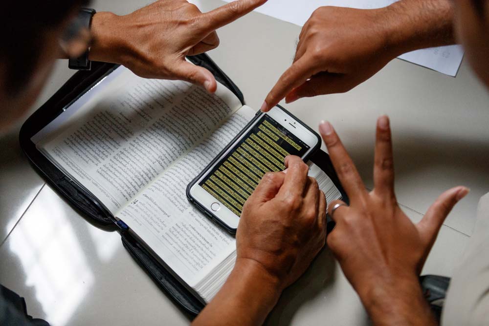 hands signing Scripture over a mobile version and printed version of the Bible